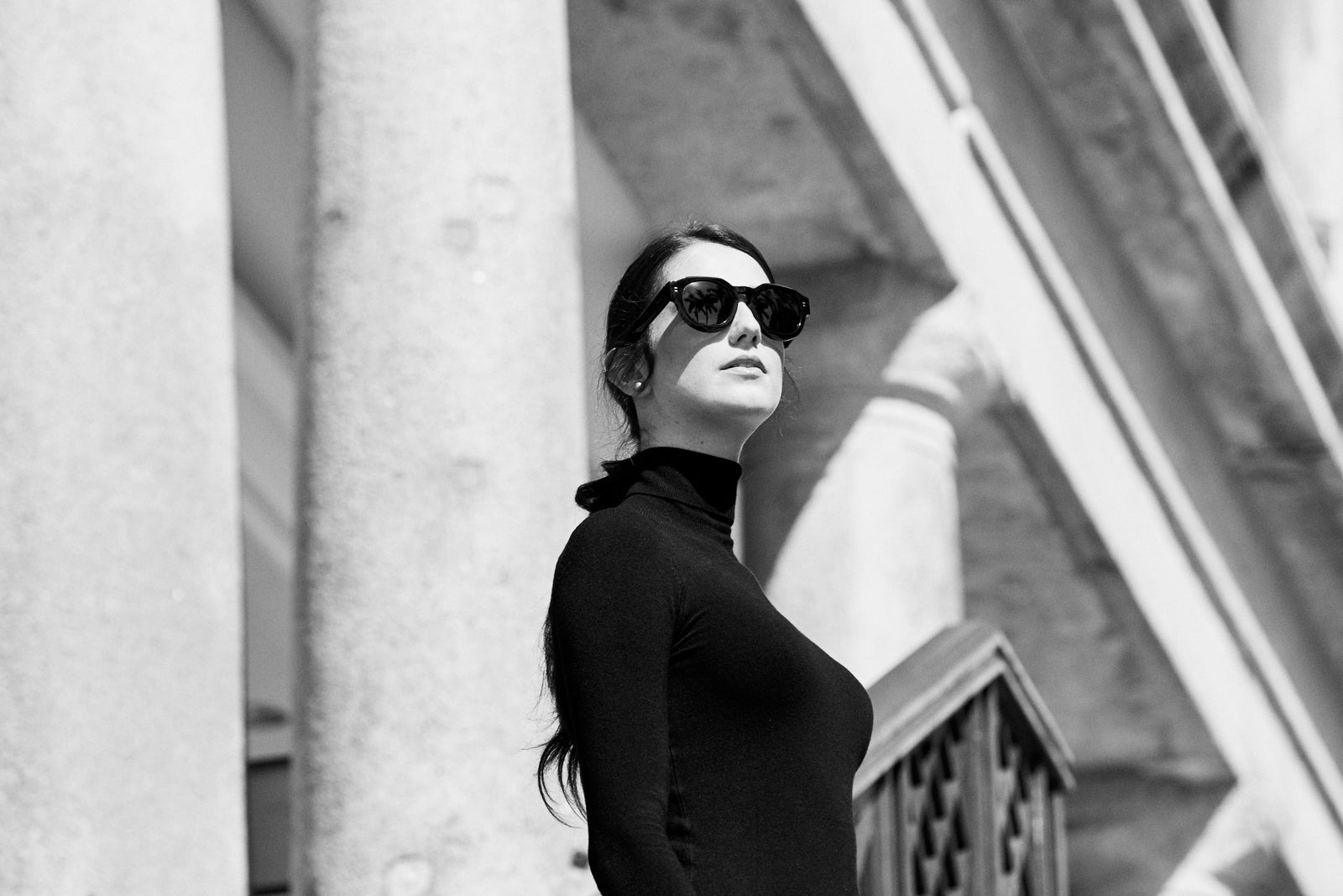 A woman in sunglasses looking up beside a column