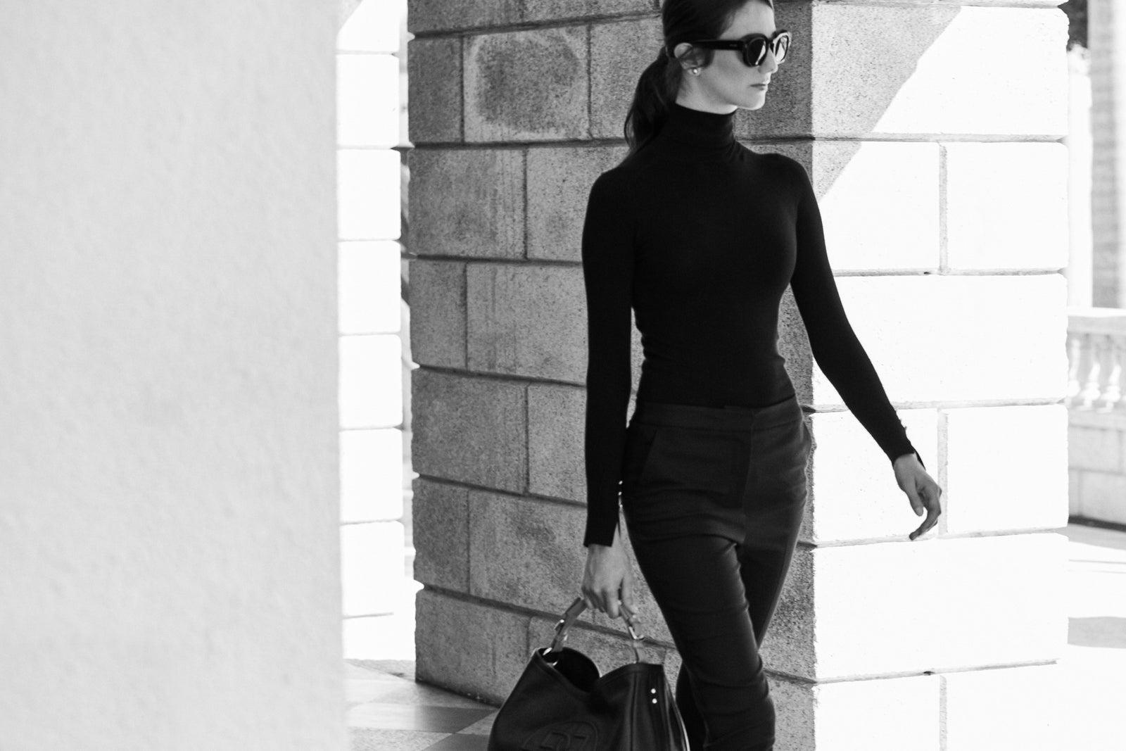 A woman in black walking past a stone pillar
