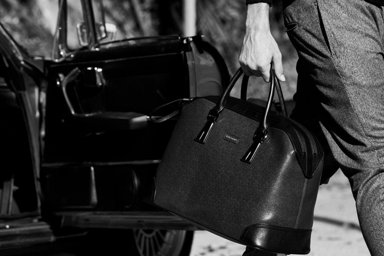A man lifting a leather travel bag from a vintage car