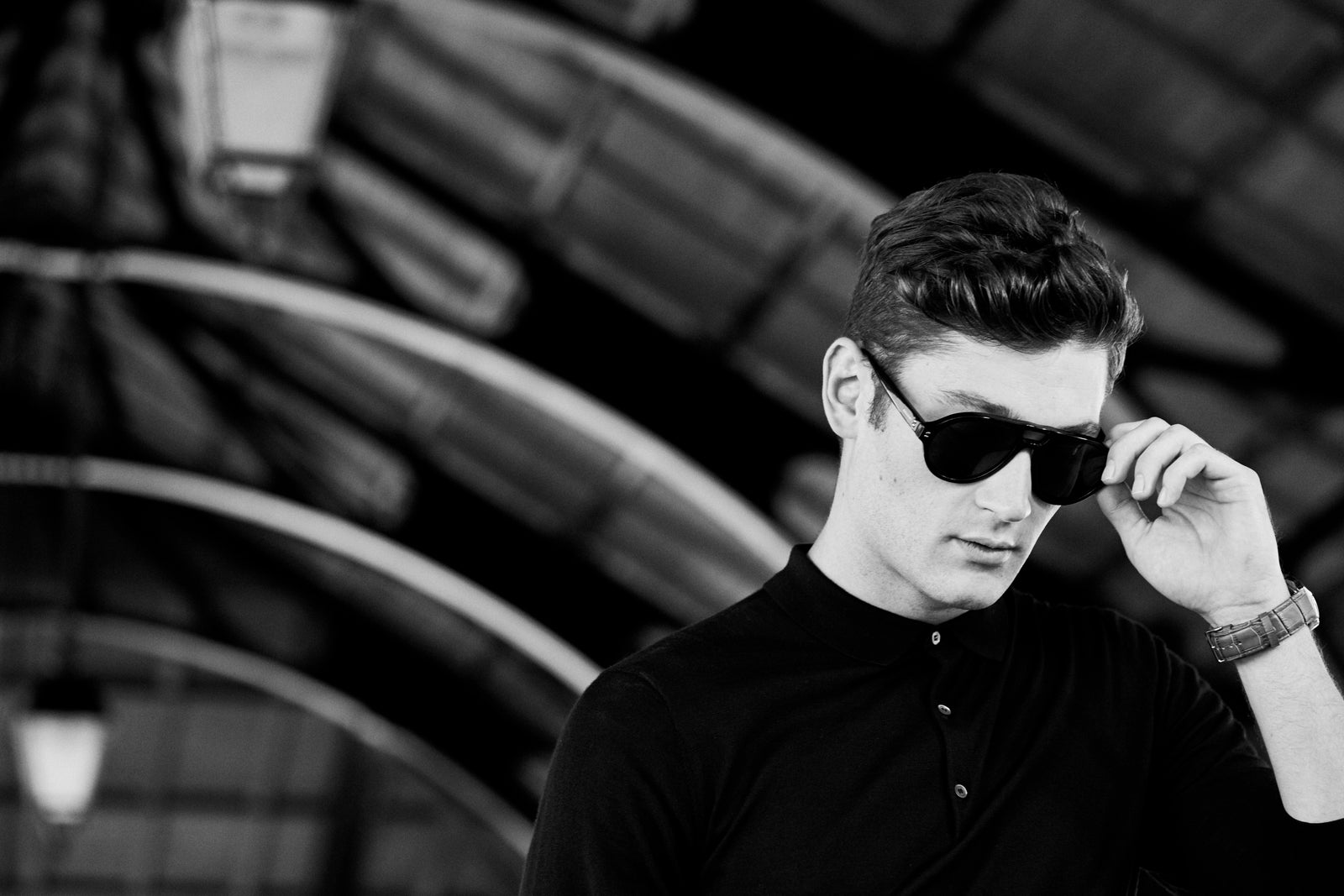 A man adjusting his sunglasses under iron arches