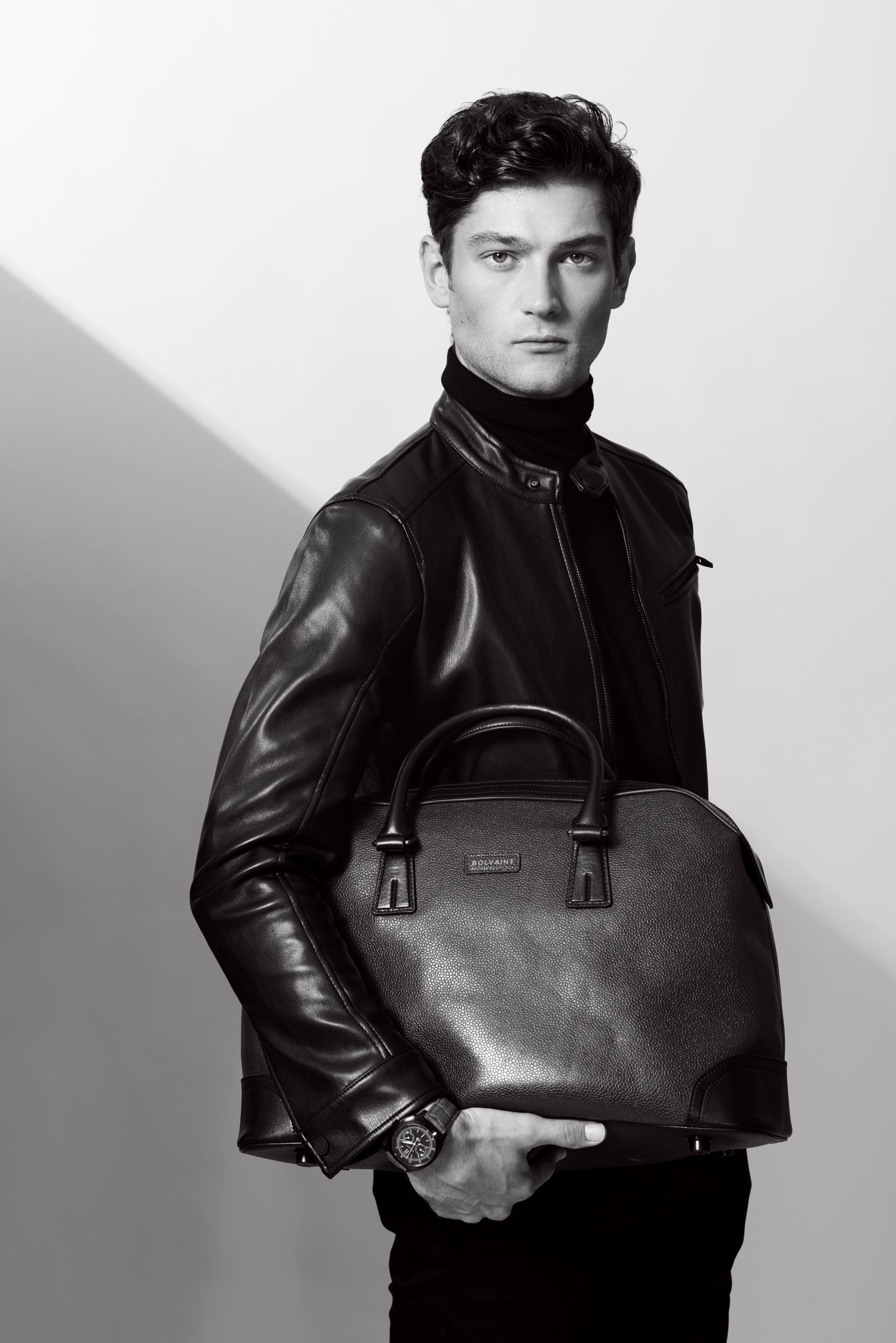 A man in a leather jacket holding a travel bag