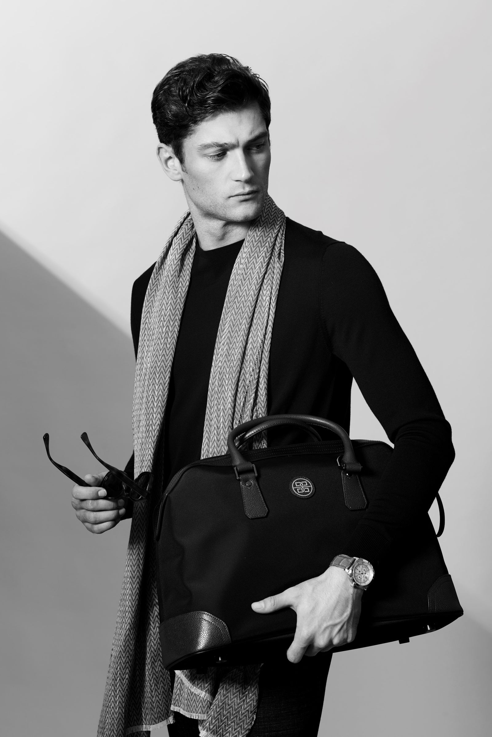 A man in a scarf holding a nylon and leather travel bag