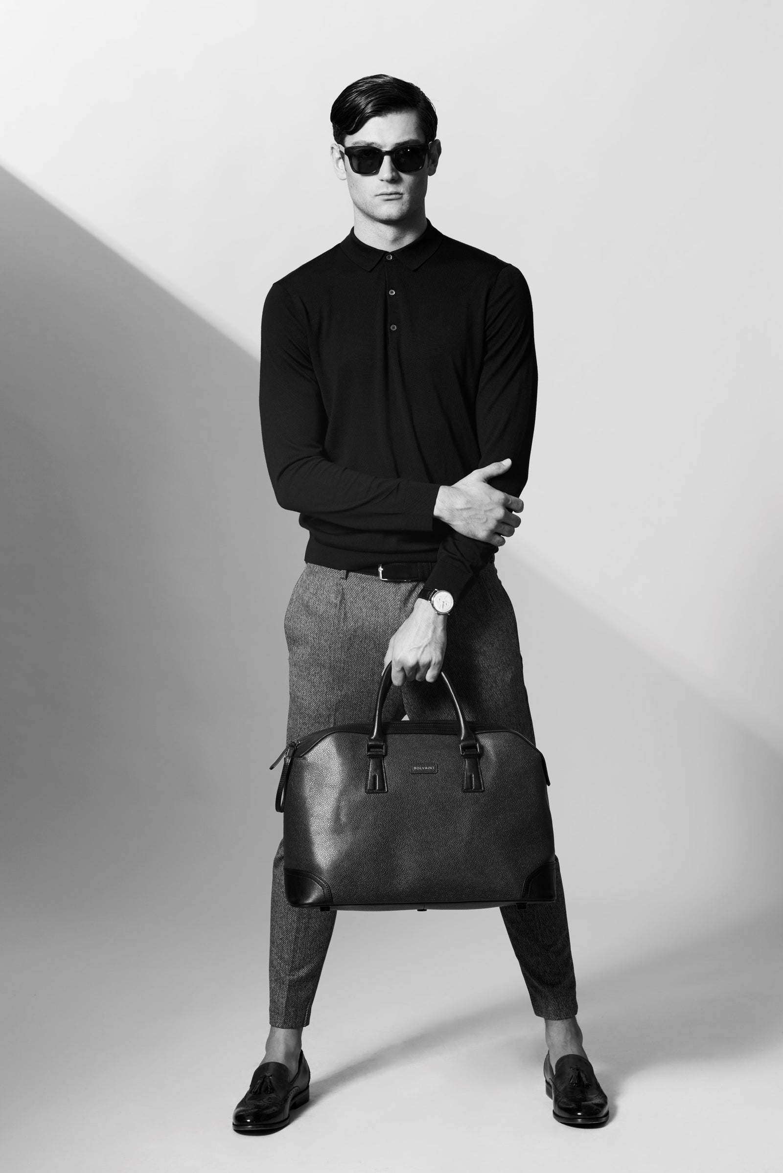 A man in black holding a leather travel bag
