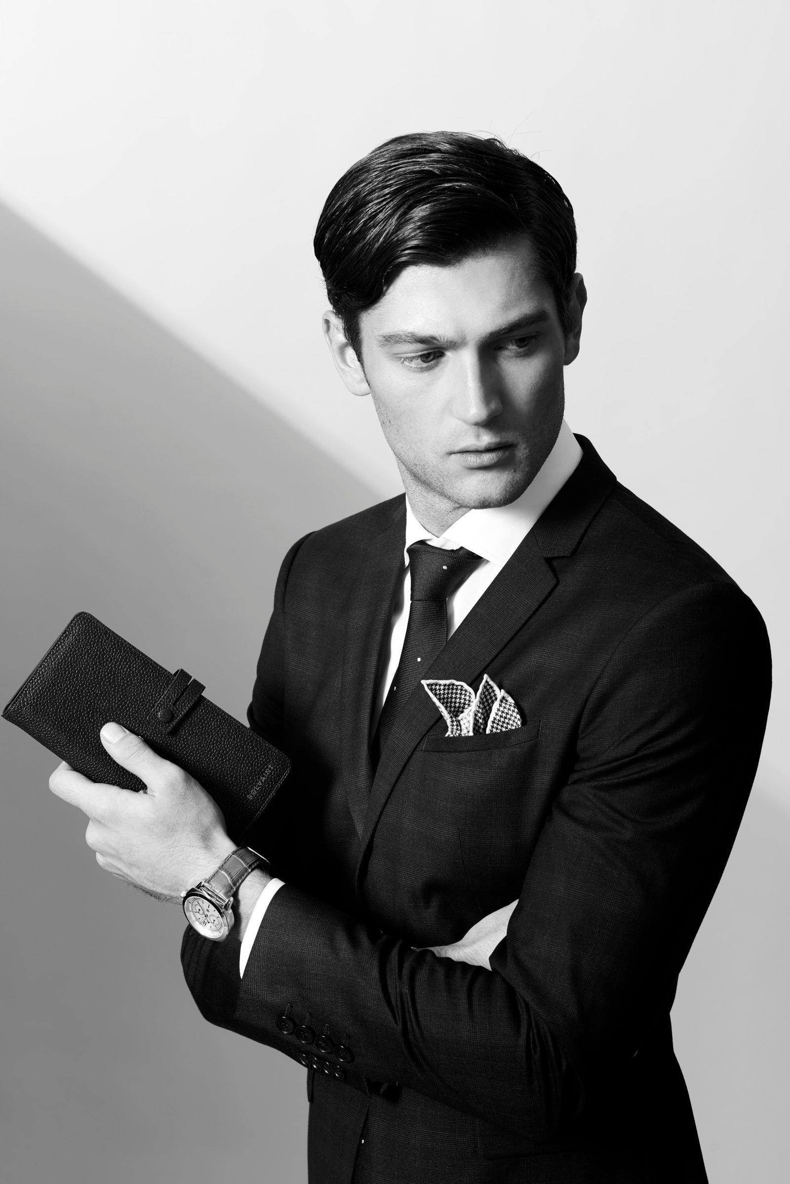 A man in a dark suit holding a leather wallet