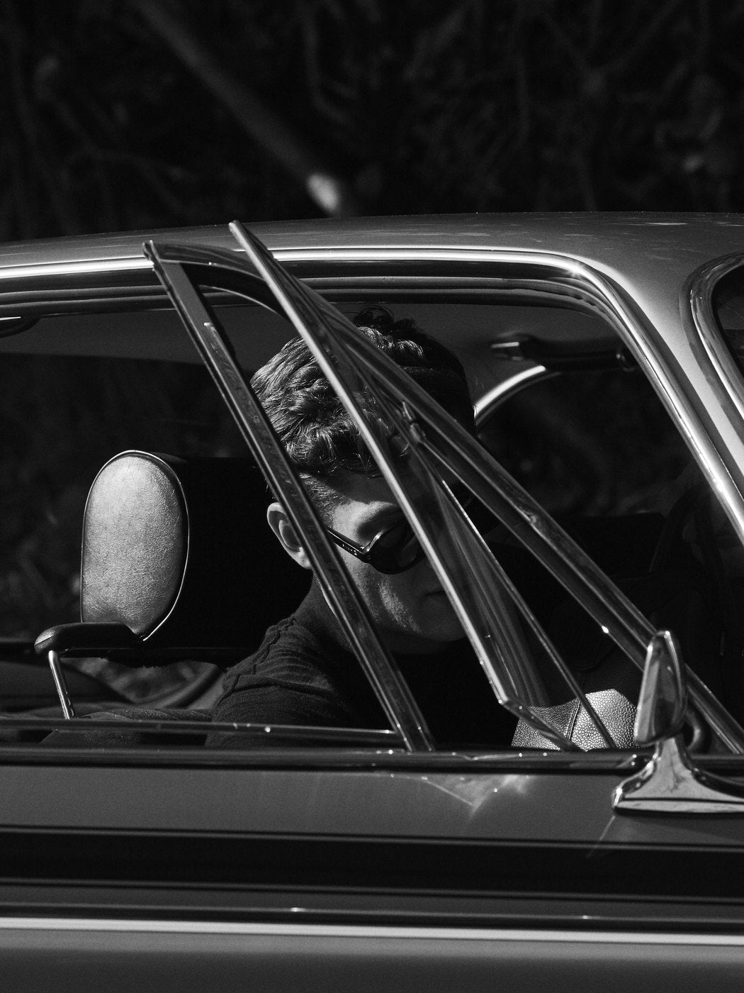 A man in sunglasses at the wheel of a vintage car